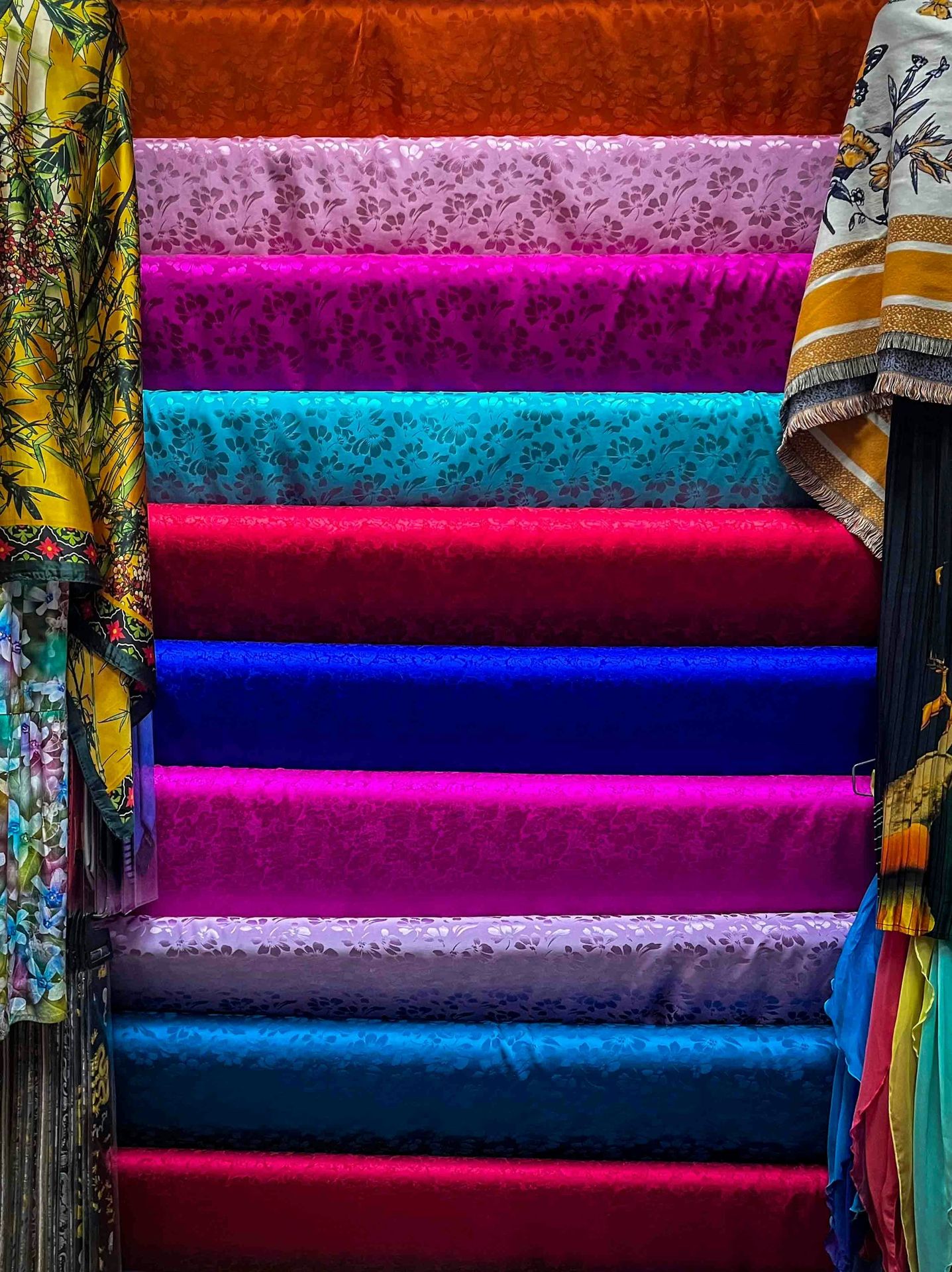 Rolls of colorful patterned and solid fabrics stacked vertically.